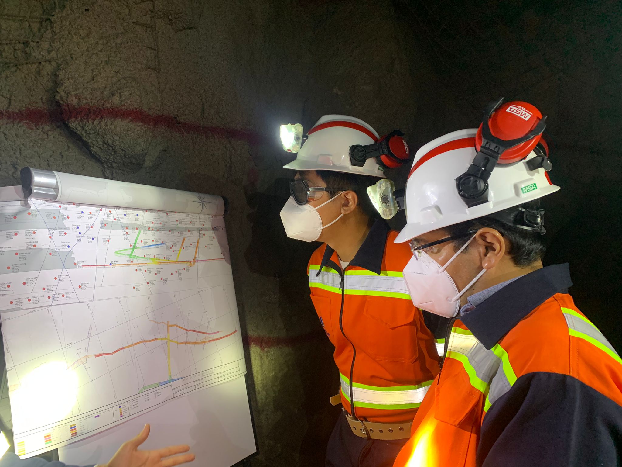 Workmen in a mine inspect a whiteboard while wearing helmets with flashlights and protective gear