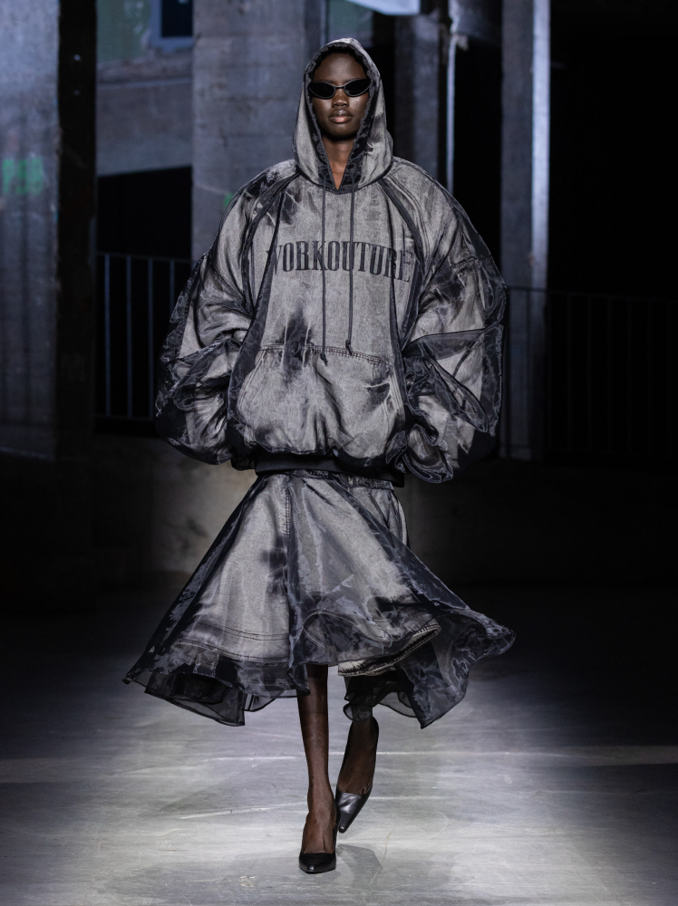 Model walks runway in Juun.J denim hoodie and knee-length skirt draped with sheer organza fabric at Paris Fashion Week