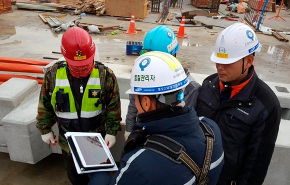 A group of construction workers from Samsung C&T discuss IoT technology on a construction site in South Korea.