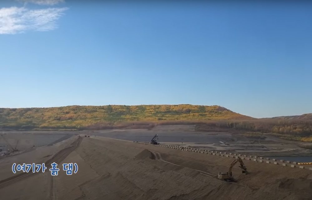 A large earth-filled dam located along a river surrounded by blue skies