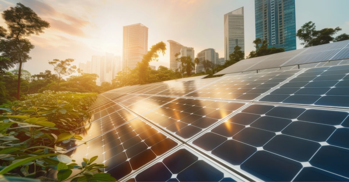 A futuristic image of a solar panel with a city skyline in the background and greenery surrounding the panels. The sun is setting in the background, casting a warm light on the reflective panels that glisten.