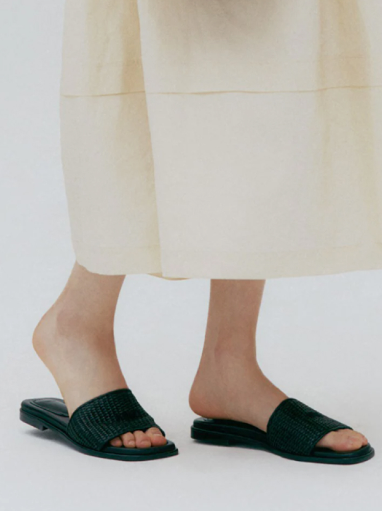 Woman wears slip on black slide shoes with a flowy cream skirt