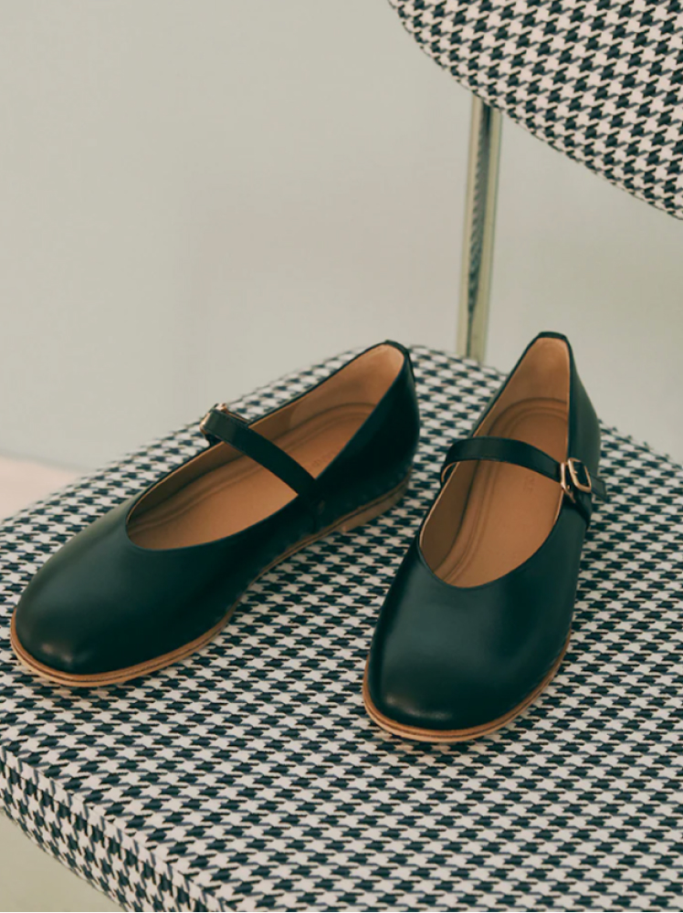 A pair of black leather mary jane shoes by the brand Beanpole sit on top of a chair with a houndstooth pattern on it.