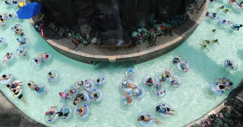 People float around a curved section of a lazy river at a water park in tubes in crystal clear blue water - Korea's Caribbean Bay Water park