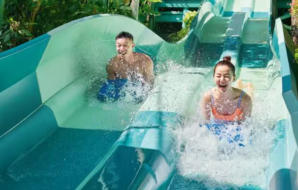 A man and a woman splash their way down the thrilling ’Dueling Racer’ water slide at Adventure Cove water park in Singapore