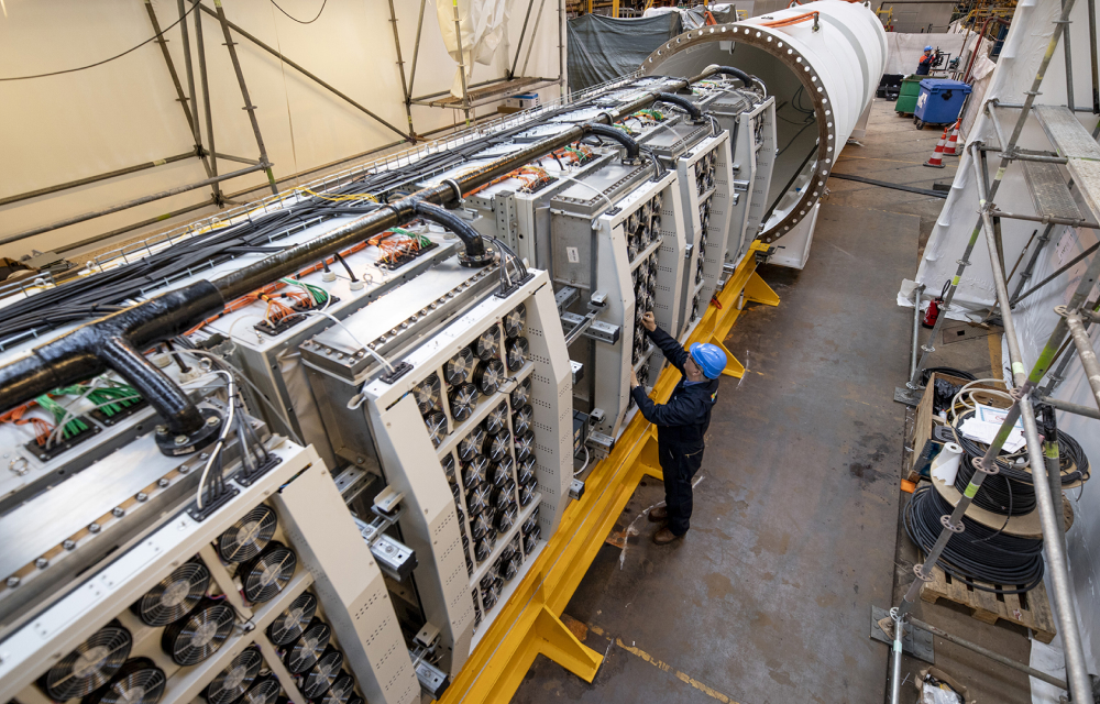 A worker inspects the inside of the Project Natick underwater data submarine among the rows of servers and pipes that connect its cooling technology and power cables.