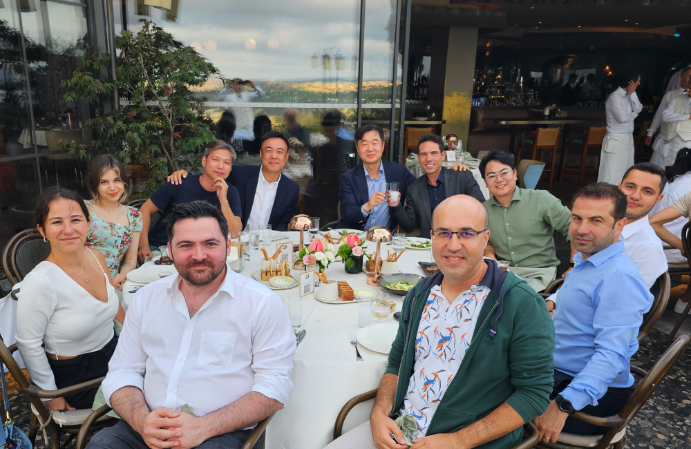 A group of office workers sit at a large outdoor table in a restaurant to share a meal together.