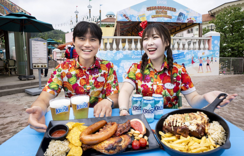 A man and a woman dressed in colorful Hawaiian shirts show off a seasonal restaurant menu with beer, sausages, chips and an assortment of side dishes placed in front of them.