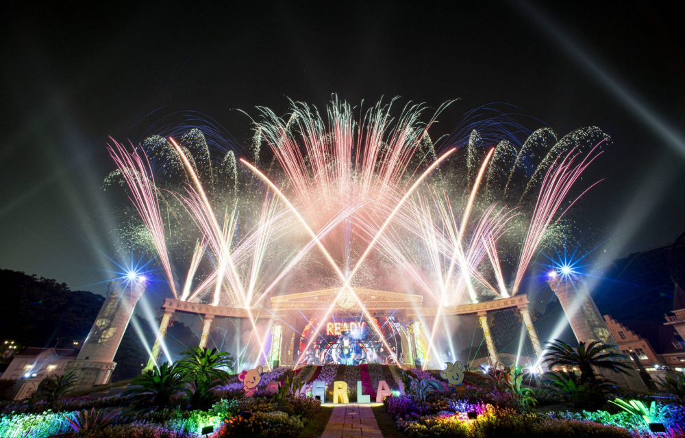 Fireworks surround a building at a theme park at night in a multimedia show.