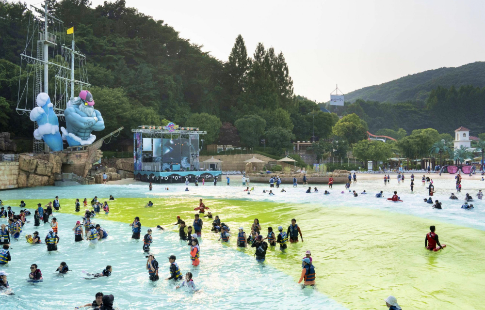 Water park goers enjoy the outdoor wave pool at Korea’s Caribbean Bay while enjoying music from a stage next to the pool with mountains in the background.