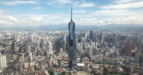 A wide shot of Merdeka 118, the towering diamond-like skyscraper standing tall in Kuala Lumpur surrounded by parks and other high-rise buildings.