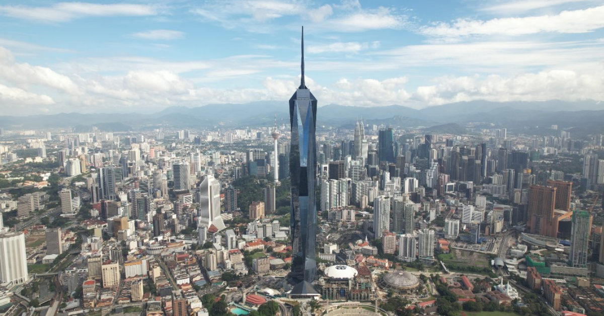 A wide shot of Merdeka 118, the towering diamond-like skyscraper standing tall in Kuala Lumpur surrounded by parks and other high-rise buildings.