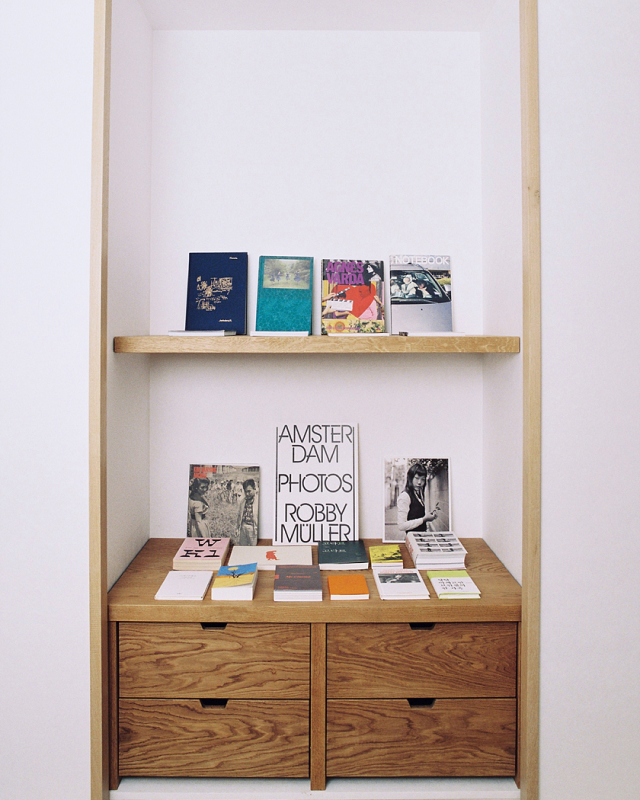 A selection of colorfully designed books in Korean and English are displayed on a simple wooden shelf.