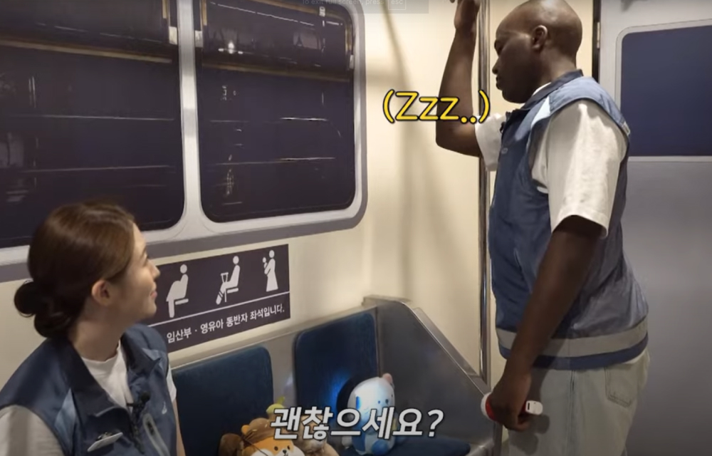 A woman sits and looks at a man standing up and sleeping while they pretend to ride a subway train in a fire evacuation experience zone at Samsung C&T’s Safety Academy