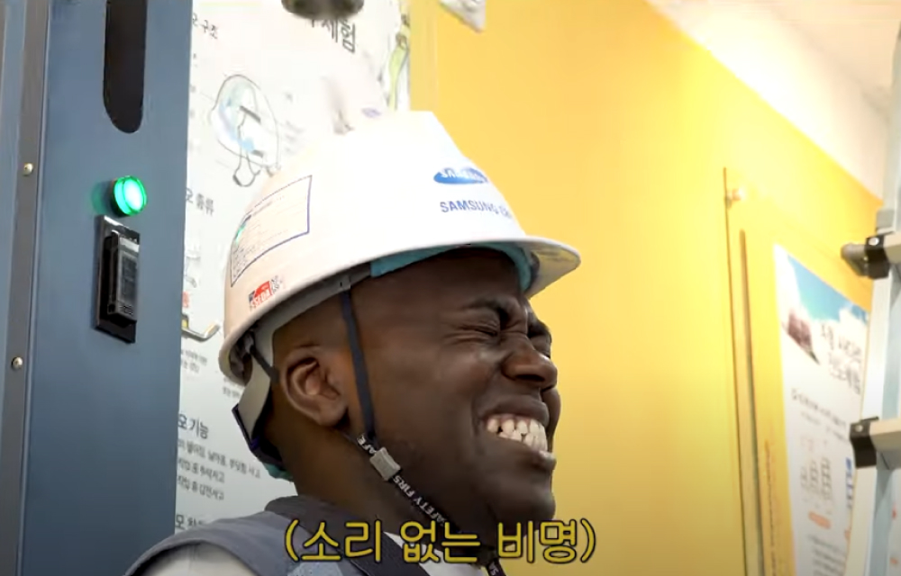 A man in a construction safety helmet grimaces as he awaits a drop from a heavy object on his head in a safety awareness exercise.