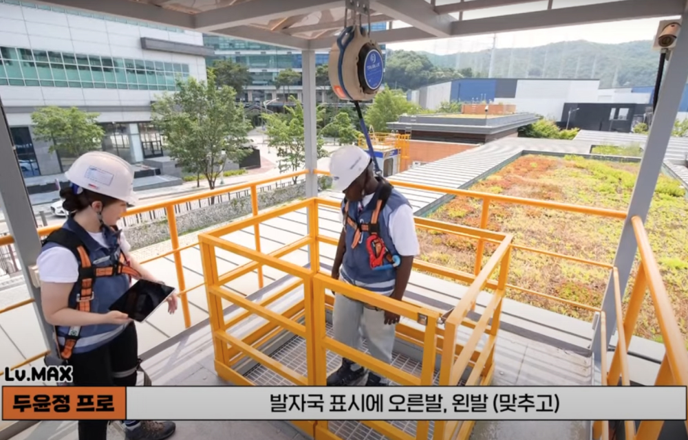 A woman and a man in safety helmets prepare for a simulation of a construction site fall while wearing safety equipment