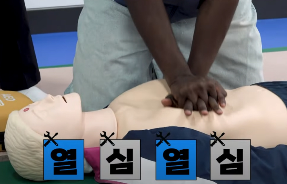 A man interlaces his hands and presses them onto the chest of a mannequin lying on the floor to practice emergency CPR.