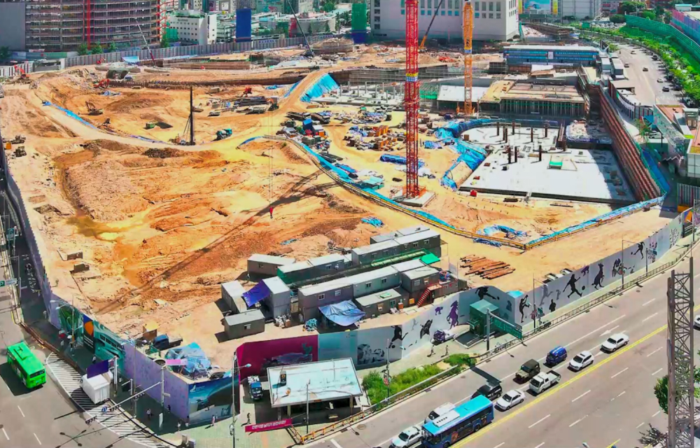 An image capturing the entire scale of Samsung C&T’s construction site for the DDP in Seoul as building preparations begin. An empty lot of land covered in sand and soil is surrounded by a fence and nearby road.