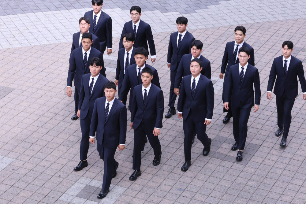 A group of 15 professional Korean baseball players walk together in a triangle formation wearing custom wool suits in a navy color, showing that Galaxy’s suits are designed for a wide range of male body types.