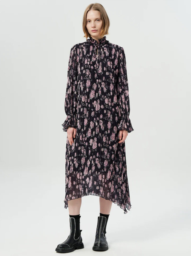 A model wears a long-sleeved black midi dress by Ganni with a pink floral print on it with ruffled details paired with black leather boots.