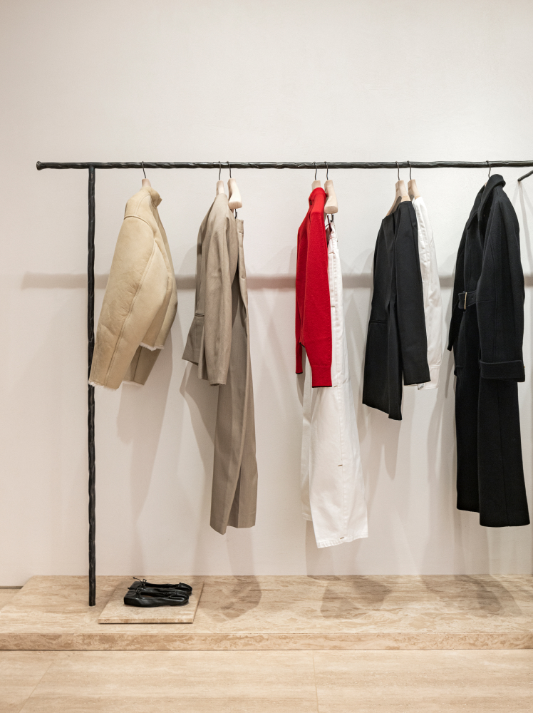 Beige, brown, red, black, and white garments hang on a simple black clothing rack in a minimally designed Jacquemus store at Shinsegae Department Store in Gangnam, Seoul.