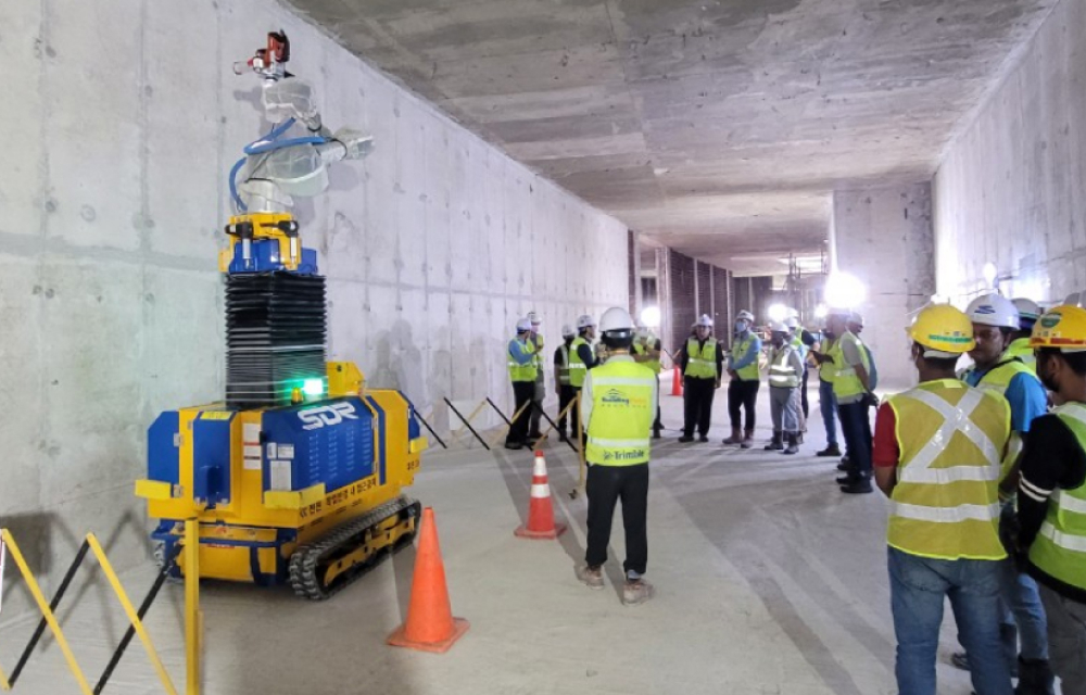 A construction site featuring the Smart Drilling Robot, a yellow and blue automated machine drilling into a concrete wall.