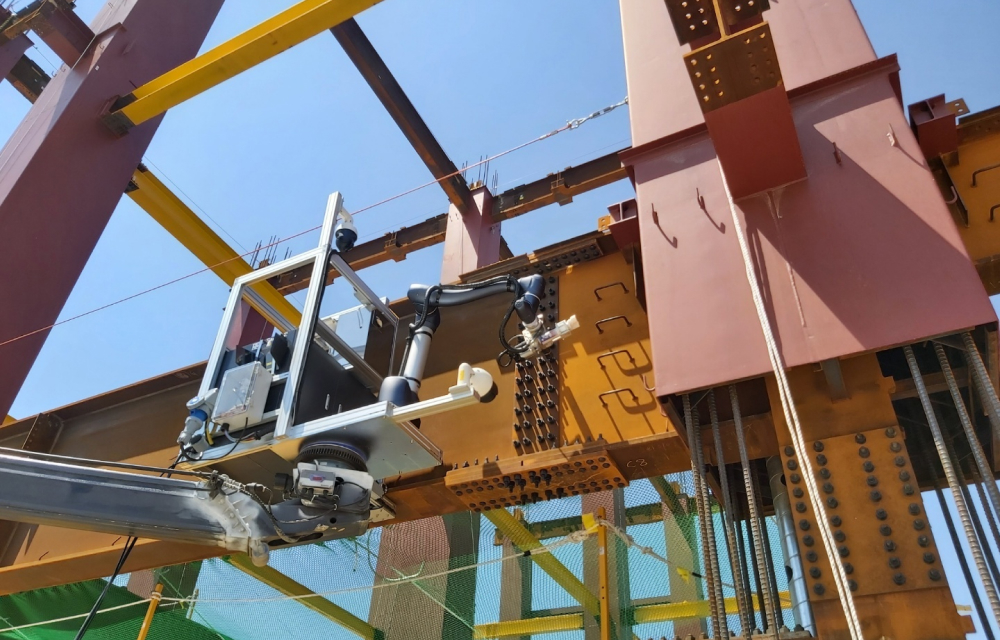 A construction site featuring an automated robot system mounted on a steel beam, performing bolt-tightening tasks. The steel structure includes yellow and brown beams, with safety nets and reinforcements visible in the background under a clear blue sky.