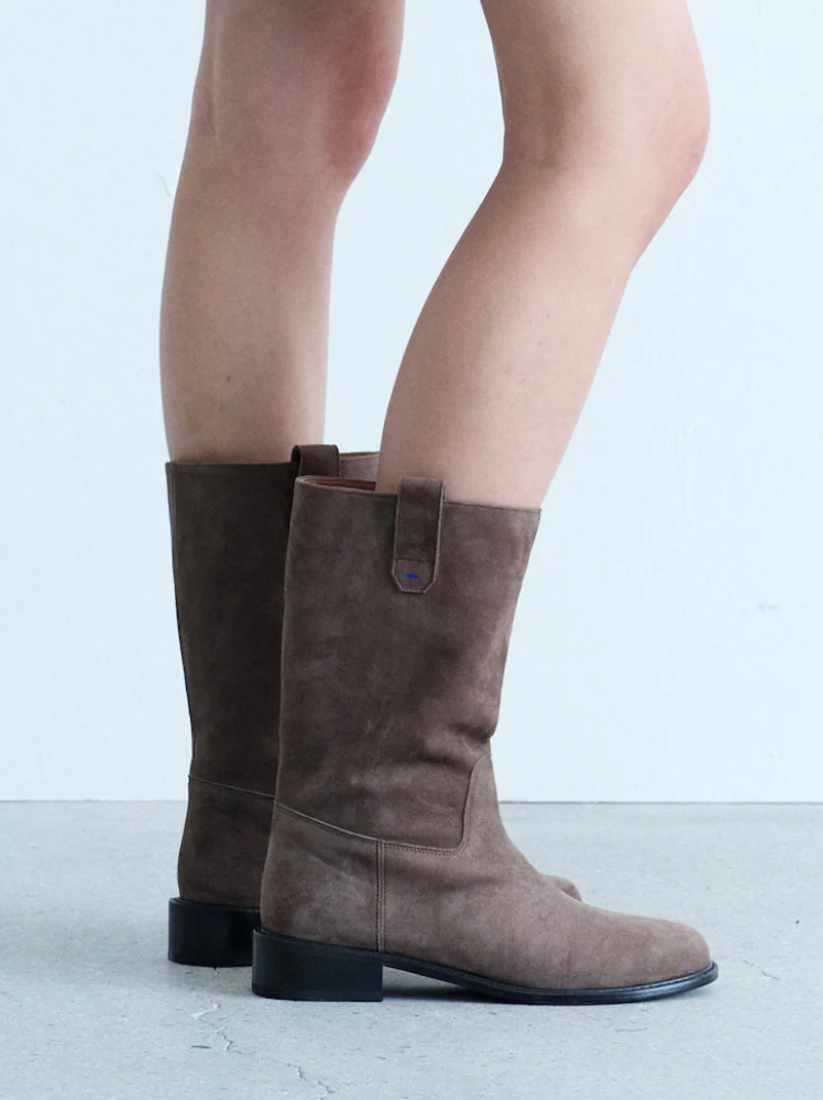 A close up of a model posing with mid-calf brown suede boots.