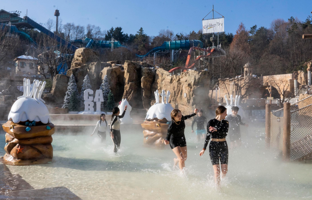 A group of guests at Caribbean Bay run toward the camera while splashing in an outdoor spa pool that is decorated with adorable characters from the Moomin series.