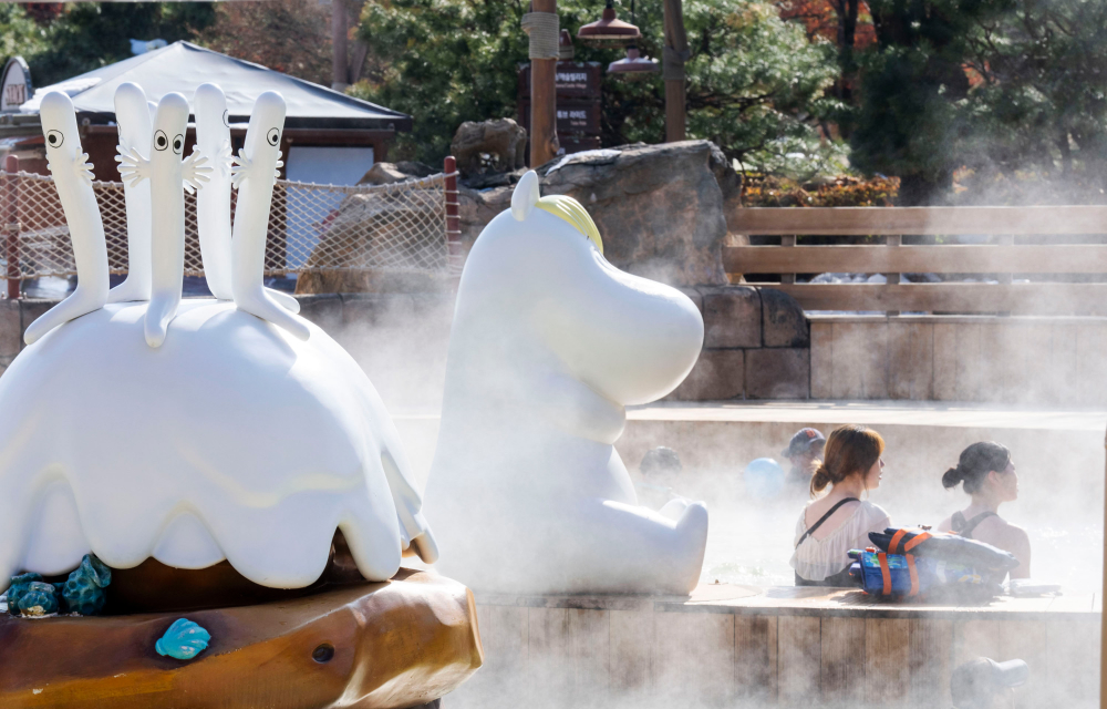 Five Hattifatteners sit on top of a cute snow-covered mountain next to Snorkmaiden who sits by the edge of an outdoor spa pool at Everland’s Caribbean Bay where visitors are enjoying a relaxing spa experience.