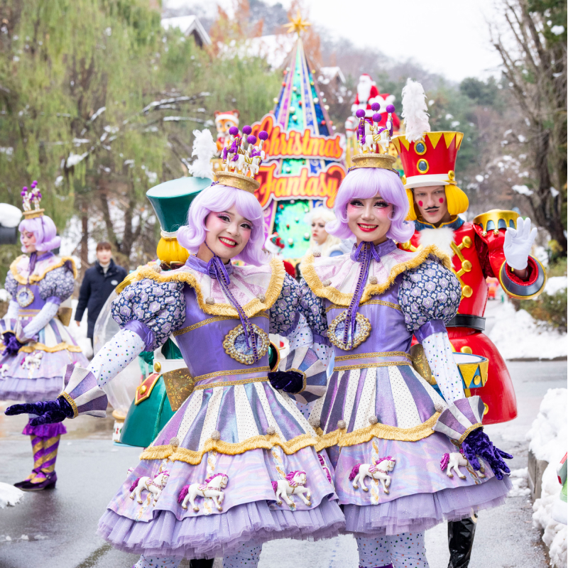 Dressed-up performers at Christmas Fantasy – Two performers in elegant lavender costumes pose near the parade float.