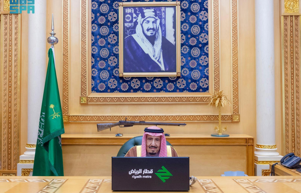 King Salman of Saudi Arabia seated at a desk labeled "Riyadh Metro," for the official launch of Riyadh's new metro system. The background includes a portrait of King Abdulaziz, Saudi flags, and ornate decorative elements.