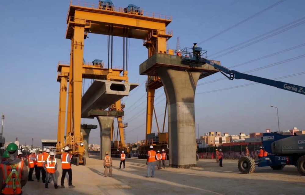 A close-up view of a Full Span Launching Method (FSLM) construction process, where a massive yellow gantry crane lifts and positions a pre-cast concrete segment for an elevated bridge or metro track.