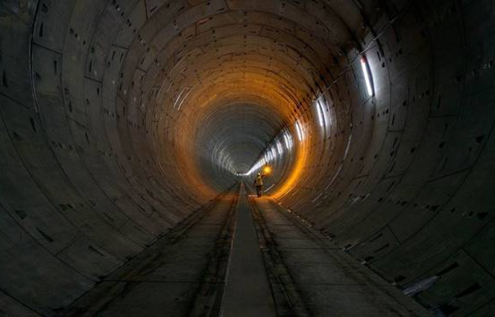 A well-lit, completed underground tunnel featuring smooth, reinforced walls and train tracks on the ground.