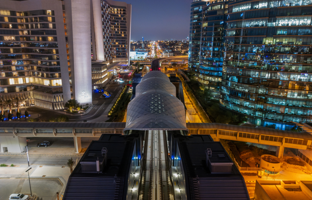 An overpass that leads up to train tracks along the Riyadh Metro in the heart of the city surrounded by beautiful modern high rises lit up at night