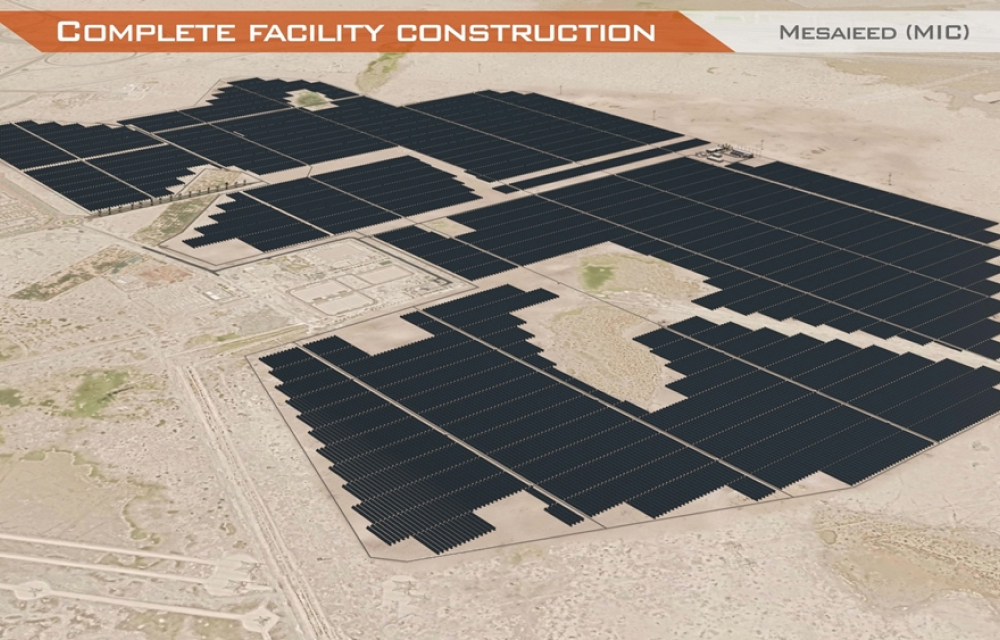 A wide aerial view of a solar farm in a desert area, consisting of vast arrays of black solar panels arranged in geometric patterns.