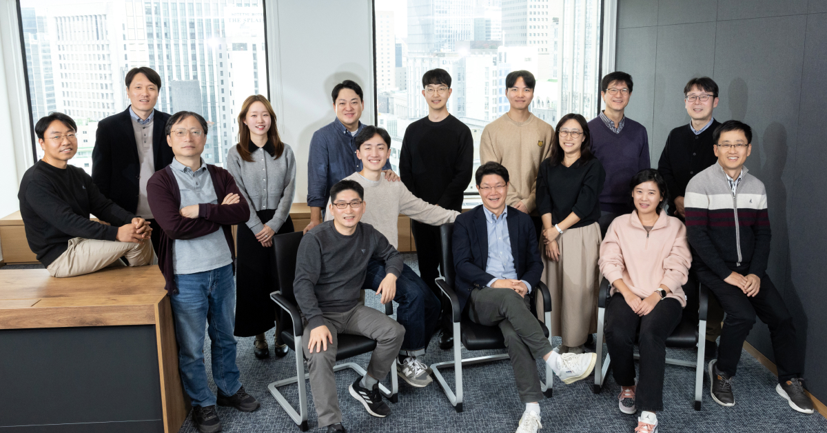 A group of team members from Samsung C&T’s Digital Innovation Group posing in a modern office setting with cityscape views in the background.