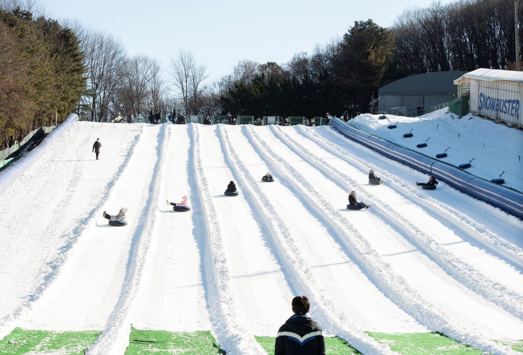 A wide view of Everland's Snow Buster Racing Course showing visitors sledding down parallel snowy lanes under a clear winter sky.