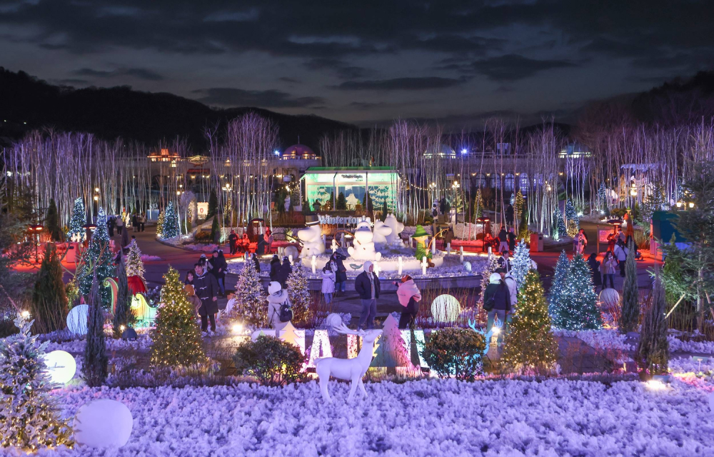 A wide-angle shot of Everland’s Nordic Forest at night, showcasing illuminated decorations, Moomin character sculptures, and visitors enjoying the enchanting atmosphere.