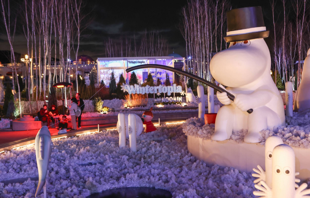 A large Moomin statue in a top hat holding a fishing rod in Everland’s Wintertopia, surrounded by glowing decorations and birch trees under the night sky.