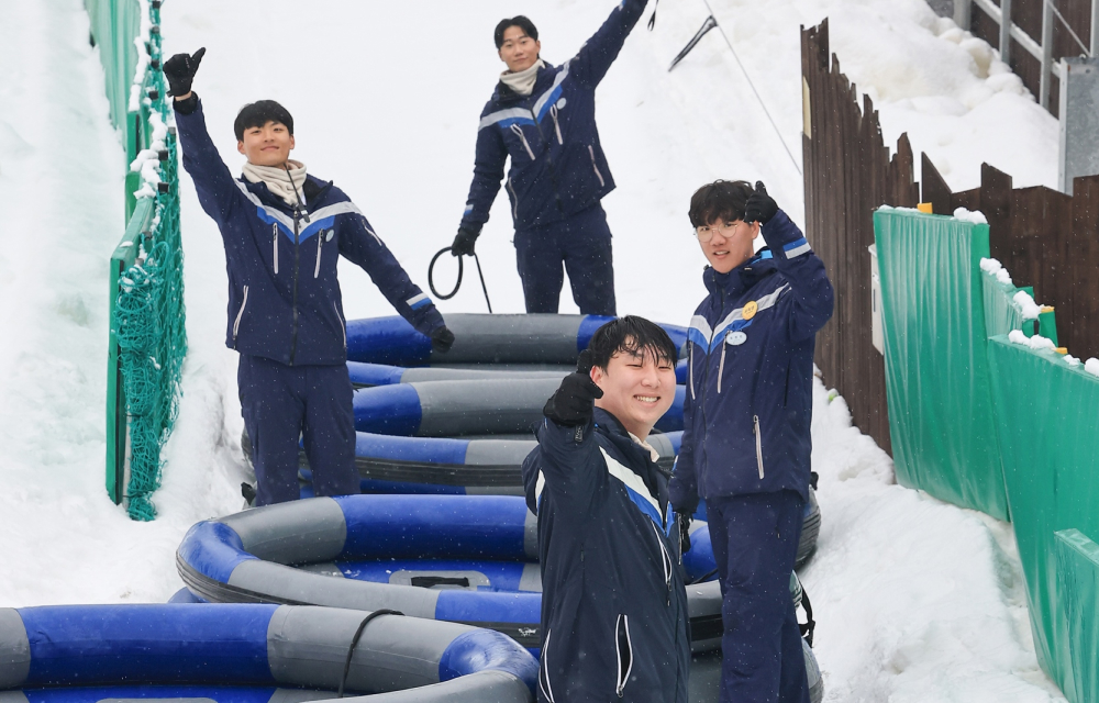 Everland staff standing beside large inflatable sleds at the Express Course, smiling and waving as they prepare for a busy day of fun-filled rides on the snow-covered slopes.