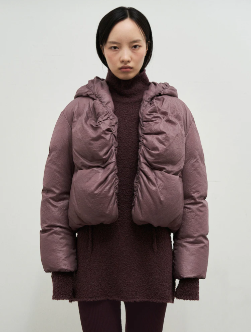 A woman wearing a ruched puffer jacket in a muted mauve color over a textured turtleneck sweater.