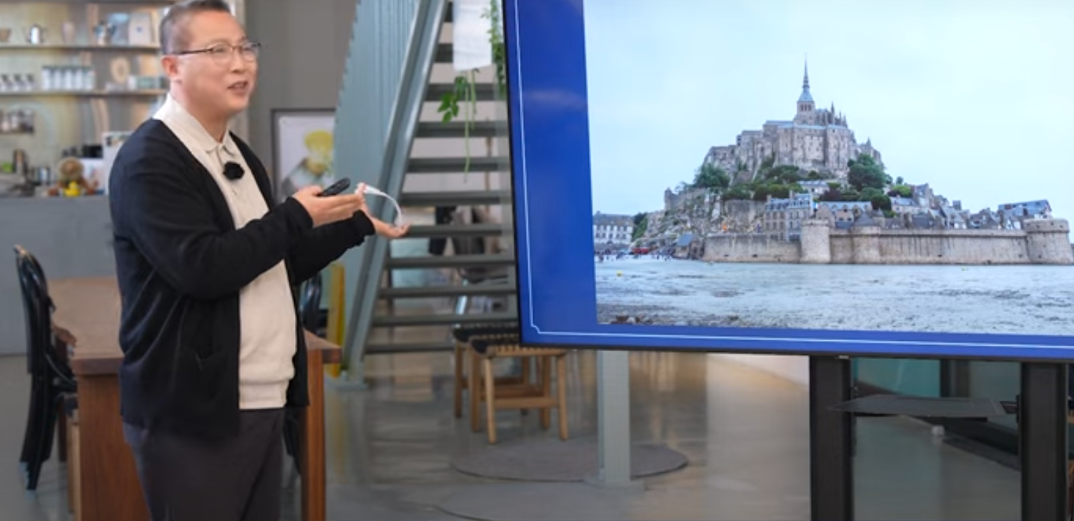 Park Wan-seo gives a presentation on historical architecture, standing beside a large screen displaying an image of Mont Saint-Michel.