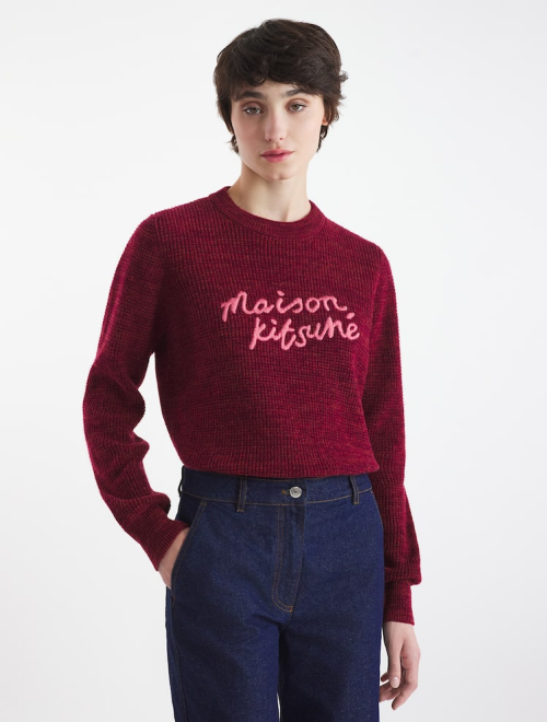 A woman in a deep red Maison Kitsuné sweater with a textured knit and dark denim jeans.