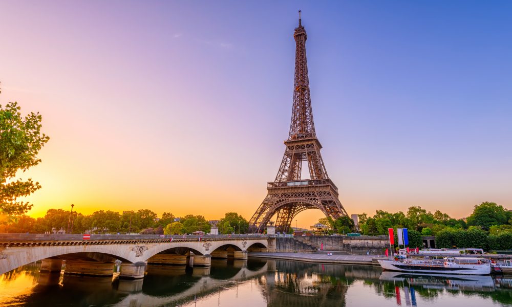 The Eiffel Tower stands tall against a colorful sunrise, reflecting in the Seine River as an iconic symbol of engineering and design.