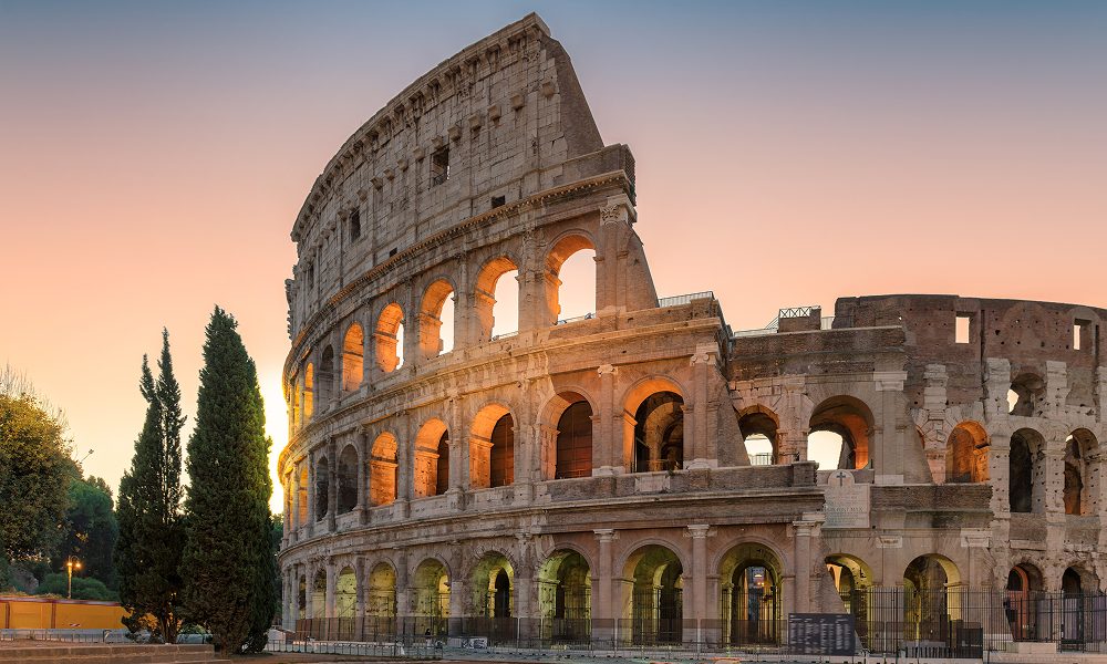 A scenic view of the Colosseum in Rome at sunset, showcasing its towering arches and ancient foundations.