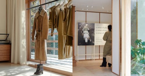 Interior of LEMAIRE’s Hannam flagship store in Seoul, featuring a warmly lit space with minimalist wooden decor, a shearling coat on display near a window, and an art installation with a person observing an exhibition panel.