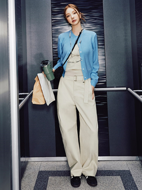 xooos stands in an elevator wearing the "Minimal Cardigan Look" from the second drop of the 8seconds x xooos collection. She styles a sky blue Edition8 Color Point Cardigan over a neutral-toned base, pairing it with beige belted cropped pants. She accessorizes with a black Sherling Mini Cross Bag and silver jewelry, holding a coffee cup and a tote for a polished yet effortless city-ready outfit.