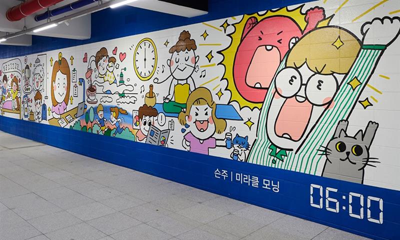 A colorful street art mural in South Korea’s longest street art gallery, depicting 6:00 AM in Seoul. The artwork features cartoon-style characters, a clock, and various lively elements illustrating early morning life in the city