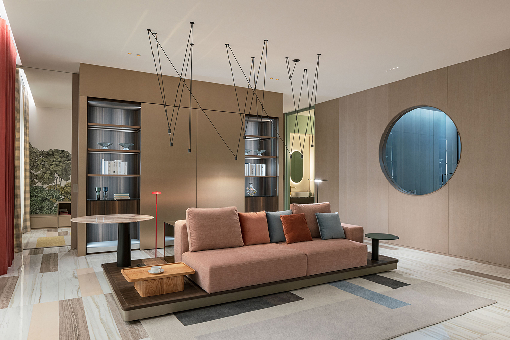 A contemporary living room envisioned in Raemian Universe, blending modern and futuristic elements. The space includes a large pink-toned sofa, sleek wooden furniture, ambient lighting, and decorative hanging rods from the ceiling, creating a warm yet cutting-edge residential atmosphere.